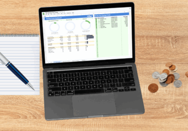 Laptop on a desk with a pen and paper and some coins