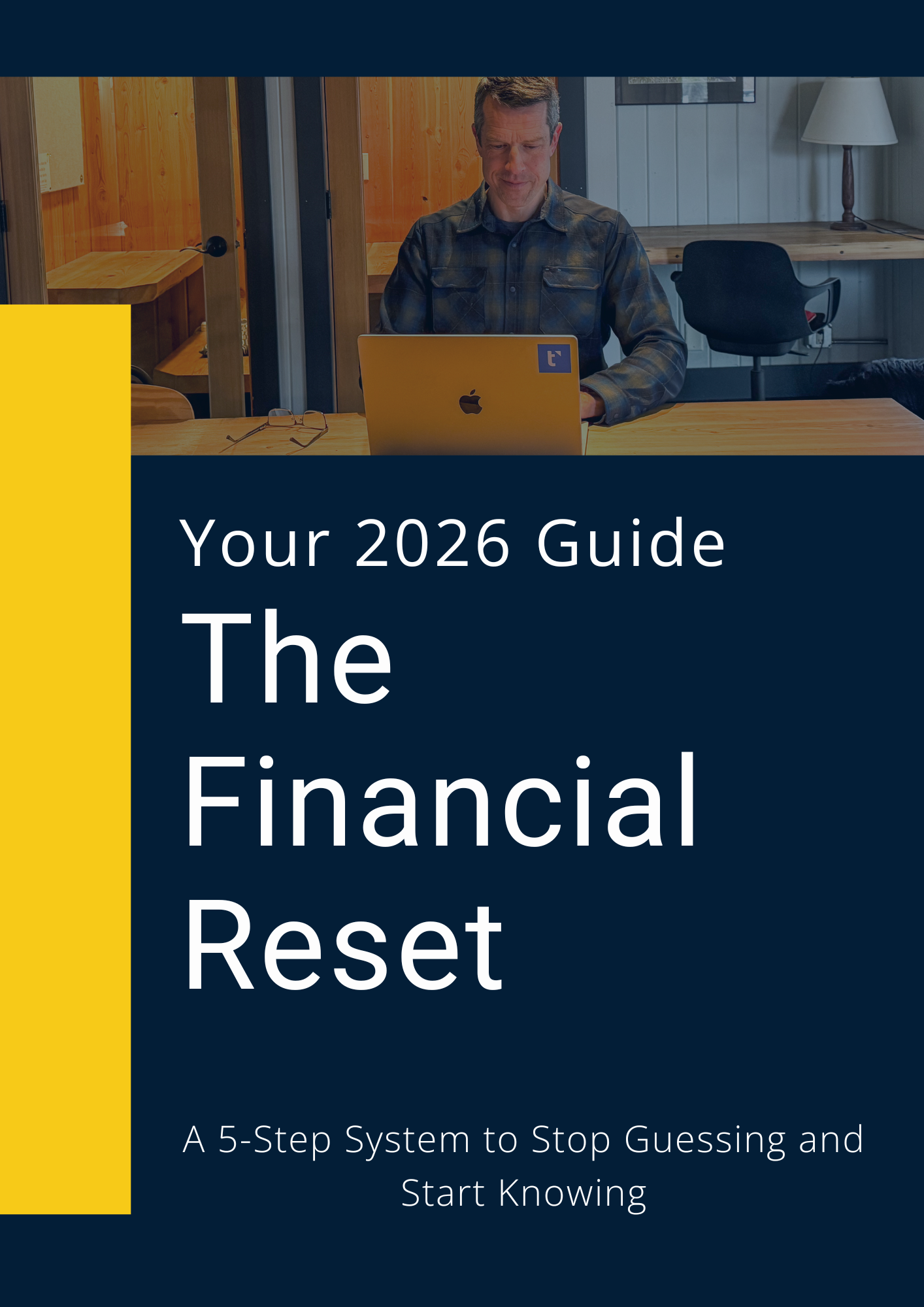 V2 The Financial Reset ebook 21 The image displays a digital book cover titled "The Financial Reset" in large white sans-serif lettering against a deep navy blue background. A bright yellow vertical stripe runs along the left edge, creating a sharp contrast with the dark background. Above the main title, smaller white text reads "Your 2026 Guide," while the bottom of the cover features the subtitle "A 5-Step System to Stop Guessing and Start Knowing." The top third of the design is occupied by a photograph showing a man sitting at a wooden desk in a wood-paneled room, looking down focused at an open laptop.