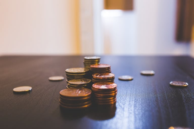 close up of various coins stacked on a dark table indoors. 144233 Close-up of various coins stacked on a dark table indoors.