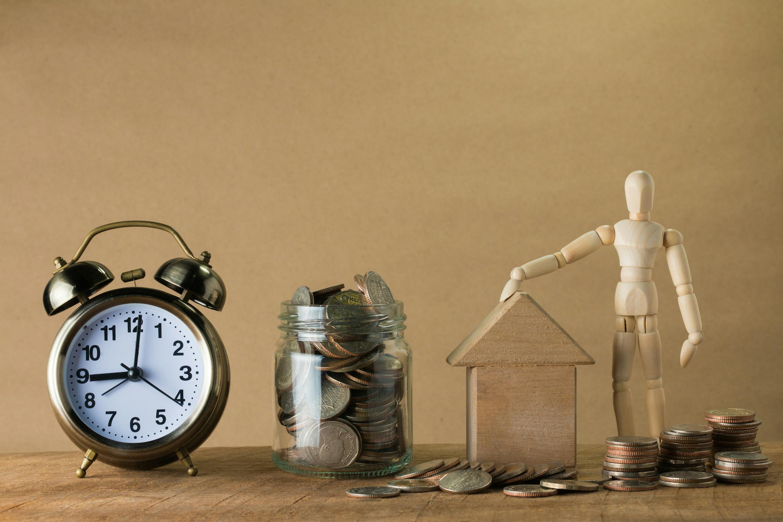 wooden mannequin with a house coins and clock symbolizing time and financial planning. 11348123 scaled Wooden mannequin with a house, coins, and clock symbolizing time and financial planning.